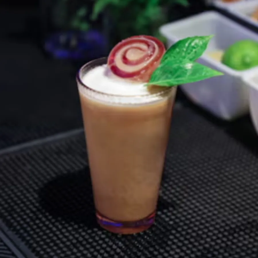 Creamy cocktail with a rolled garnish and green leaves.