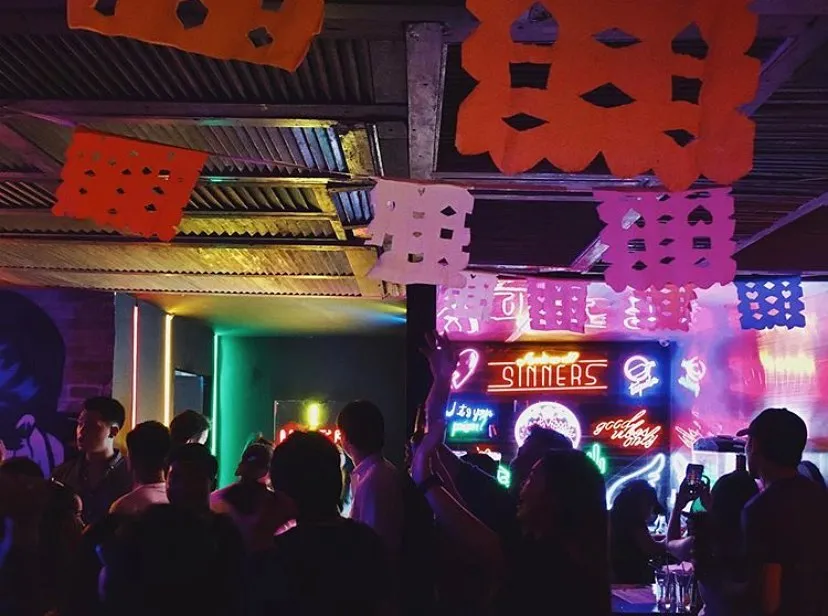 Crowd beneath colorful papel picado and neon lights inside Almacen at night.