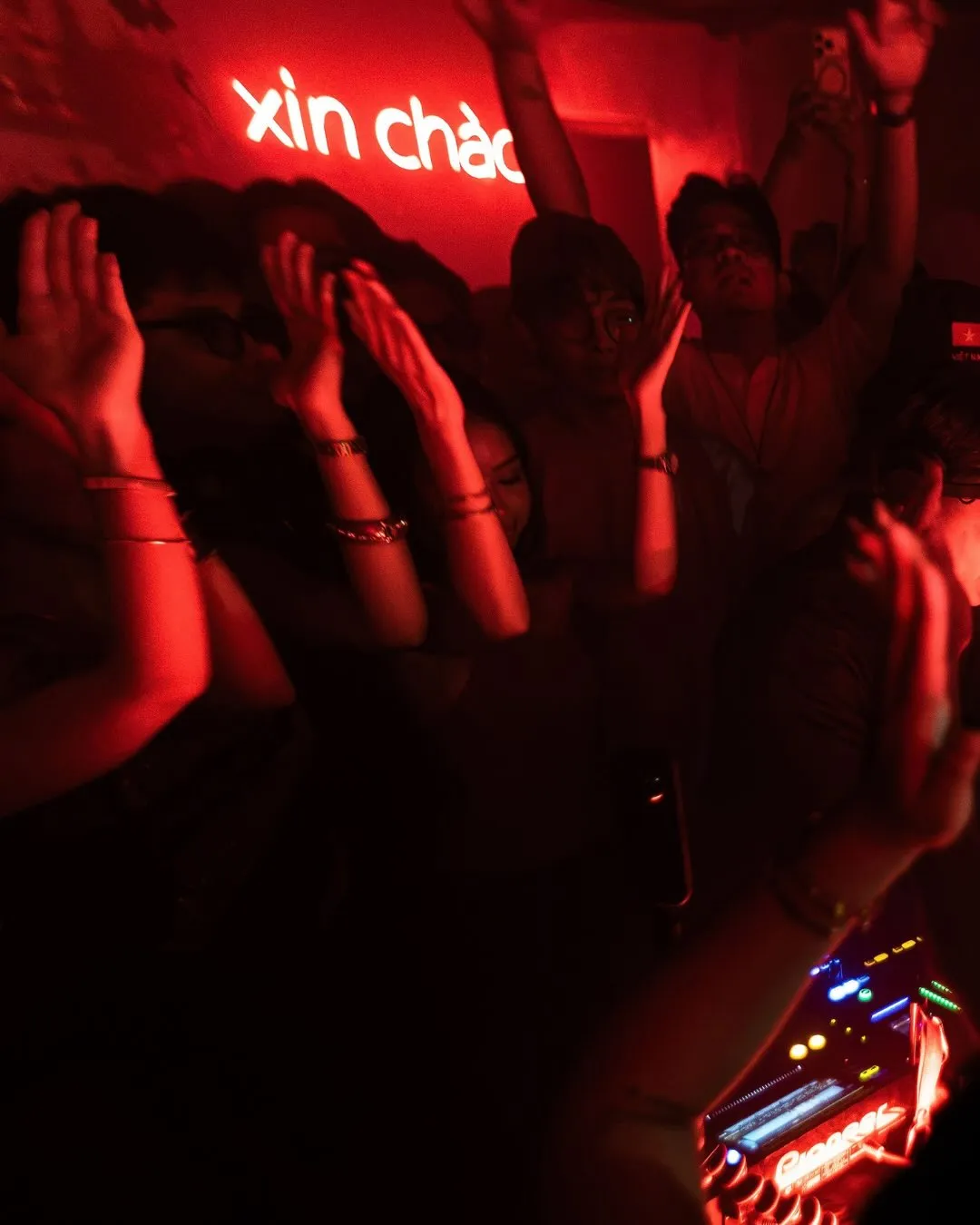 A red-lit crowd dancing beneath the Xin Chào wall sign.