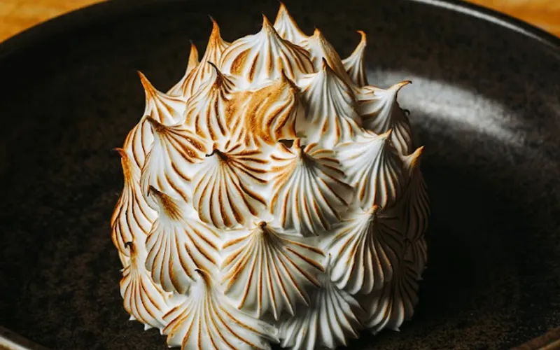 Toasted meringue dessert plated in a dark bowl.