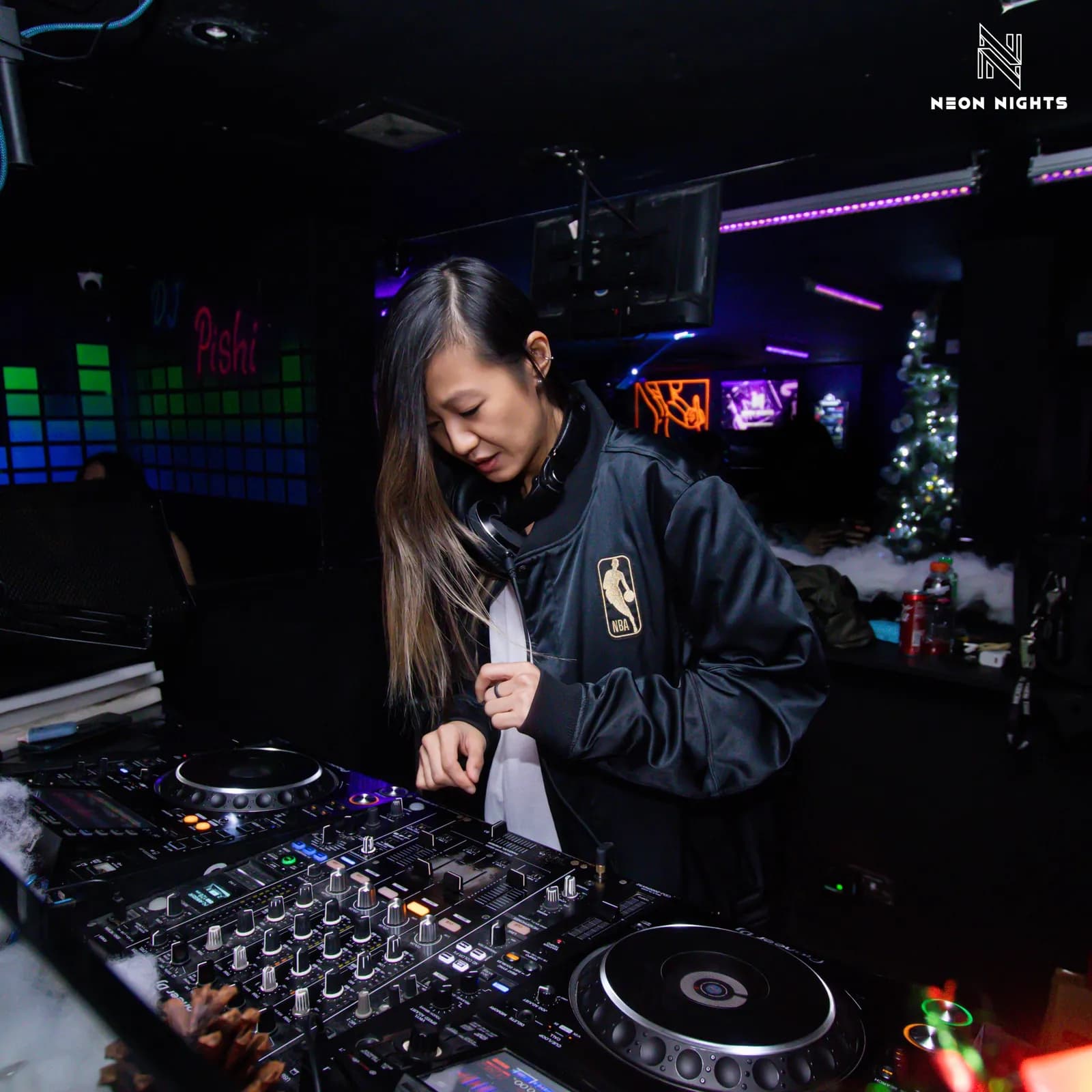 DJ working behind a full mixer under purple club lighting.