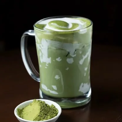 Iced green tea latte in a glass mug with matcha powder beside it.