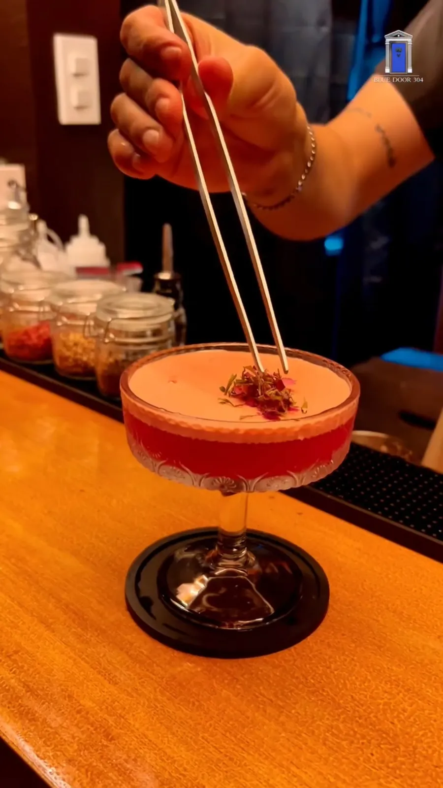A bartender garnishing a red coupe cocktail.