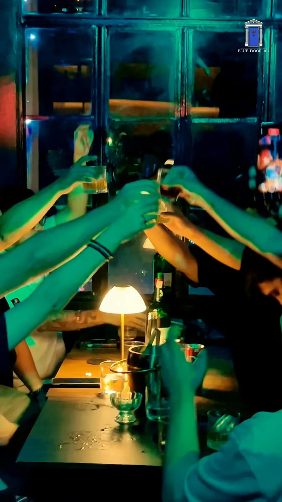 Patrons toasting across a lamp-lit table under teal lighting.
